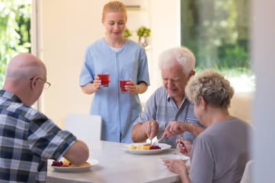 seniors eating with a young nurse with juice in glasses