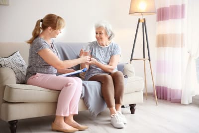 caregiver giving glass of water to senior woman