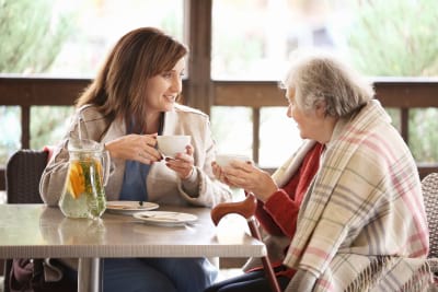 senior women and young caregiver drinking tea at table