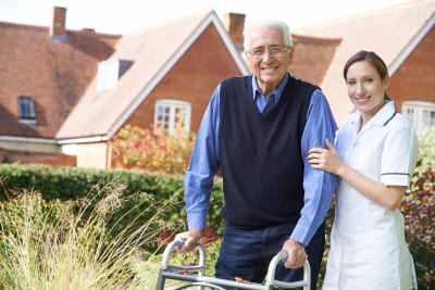 caregiver helps senior man to walk in garden